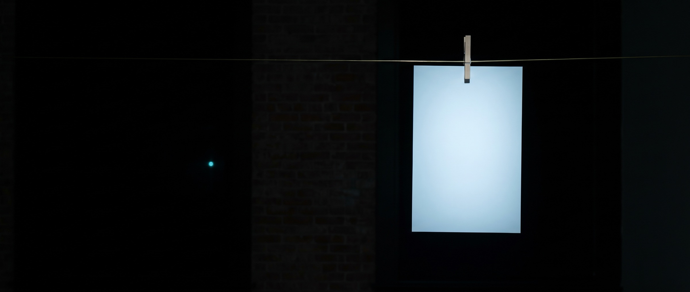 A single glowing photographic print hanging in darkness